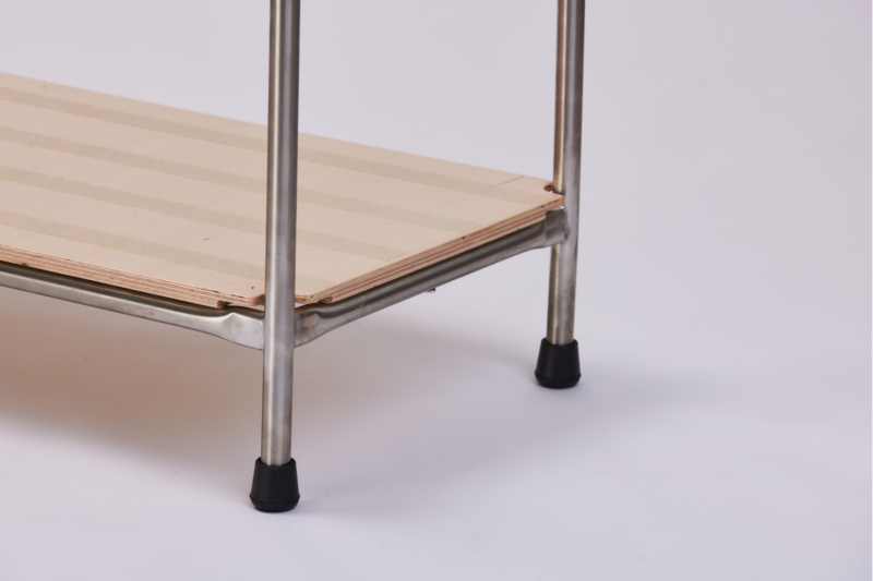 A close-up image of the corner of a metal frame stand, showcasing the wooden platform supported by metal legs. The legs have black rubber caps for stability. The wooden platform has a striped pattern. The background is plain white.