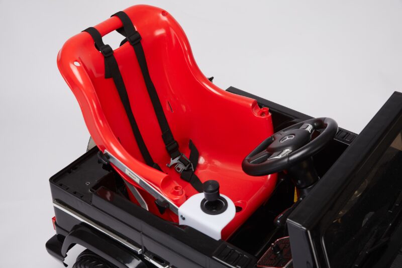 A red plastic seat with black harness straps, attached to a small black car with a steering wheel and joystick control on the right side.